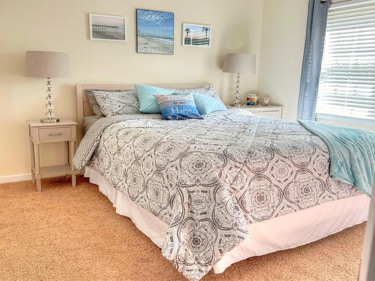 A queen bedroom featuring a neatly made bed with patterned bedding and decorative pillows. Lamps on bedside tables and framed photographs add warmth and personality to the space, inviting guests to unwind.