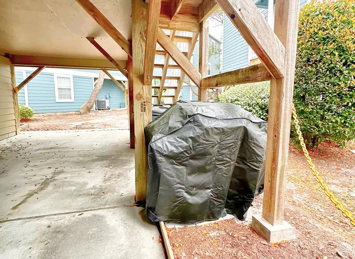 A covered grilling area located under the elevated cottage, with a staircase leading down and greenery enveloping the space. The grill is ready for use, making it perfect for hosting social gatherings and barbecues.