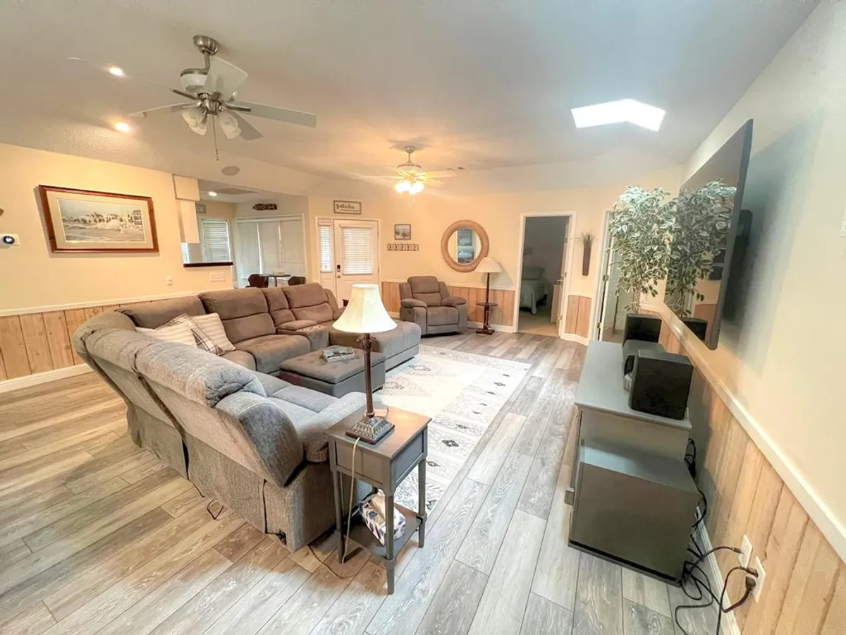 A cozy downstairs living area featuring a comfortable sofa, ceiling fan, TV, decorative mirror, and wooden paneling. The space is arranged for casual gatherings, relaxation, and entertainment, evoking a welcoming and multi-functional atmosphere.