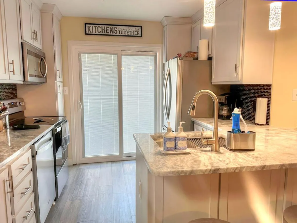A spacious kitchen with a central island, modern appliances, sliding glass door leading outside, and a decorative sign. The space is optimized for family gatherings, cooking, and easy access to outdoor recreation.