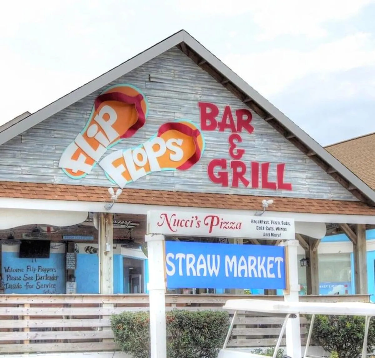 A dynamic exterior scene showcasing the Flip Flops Bar & Grill sign, Nucci's Pizza sign, and Straw Market sign. The image hints at a variety of nearby dining and shopping options, with a lively and fun neighborhood feel.
