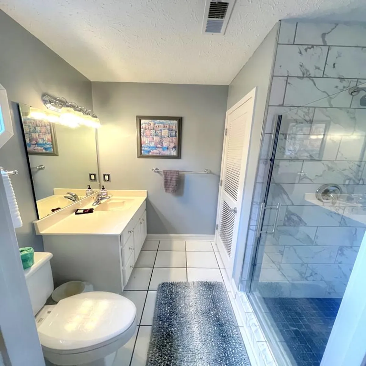 A modern bathroom with a double vanity sink, glass shower enclosure, and tasteful wall art. The room is bathed in natural light, creating a refreshing and clean environment for guests to prepare for the day or unwind at night.
