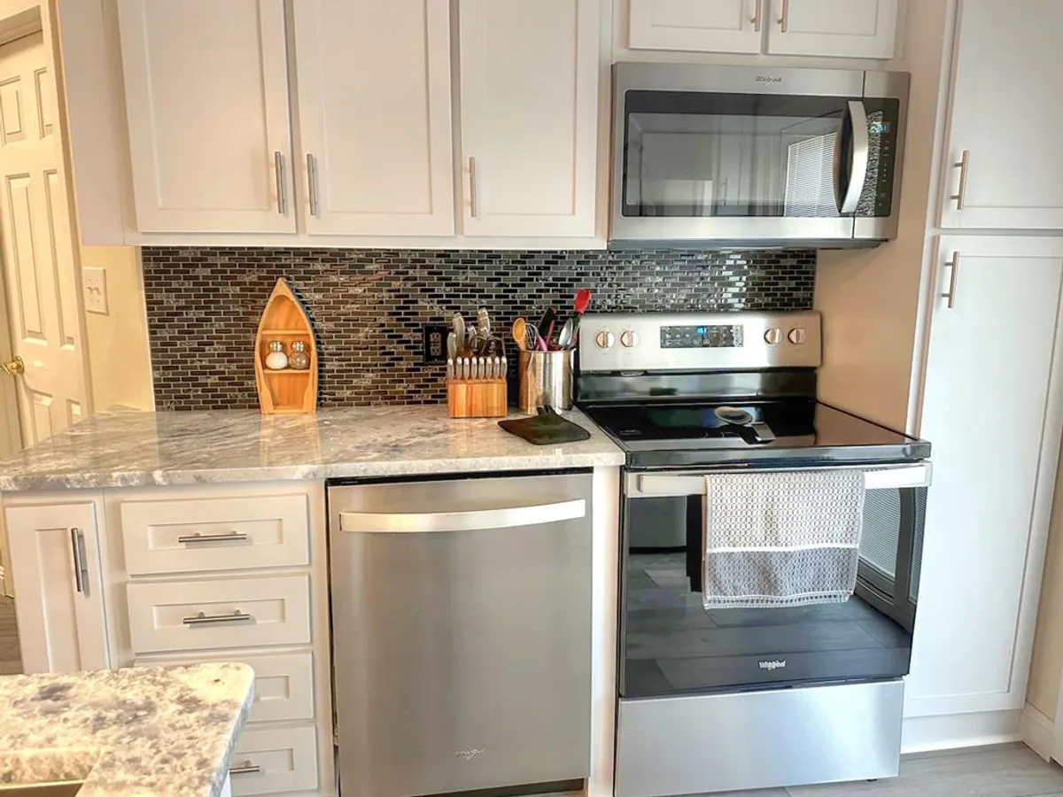 A close-up view of the kitchen highlights granite countertops, stainless steel appliances, a mosaic backsplash, and essential cooking utensils. The space feels modern and cheerful, ready for family gatherings and culinary adventures.